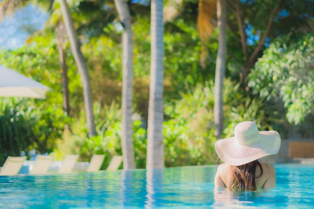 Foto gratuita il sorriso felice della bella giovane donna asiatica del ritratto si rilassa intorno alla piscina all'aperto nella località di soggiorno dell'hotel