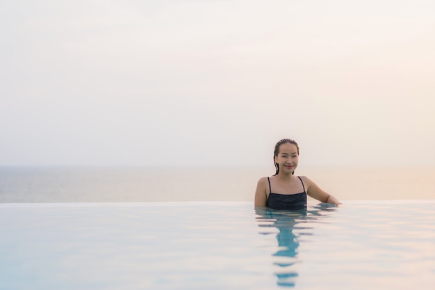 Улыбка красивой молодой азиатской женщины портрета счастливая ослабляет вокруг бассейна в курорте гостиницы