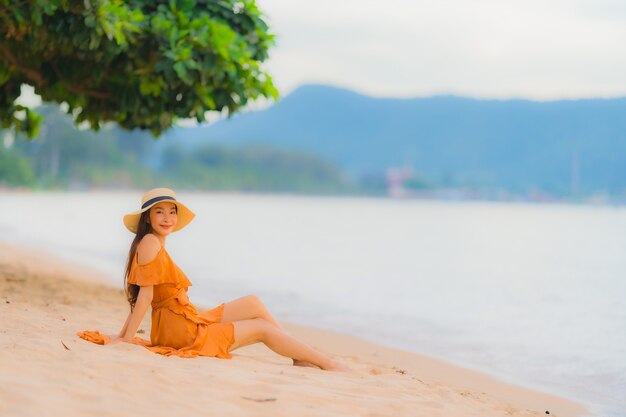 Улыбка красивой молодой азиатской женщины портрета счастливая ослабляет на океане моря пляжа