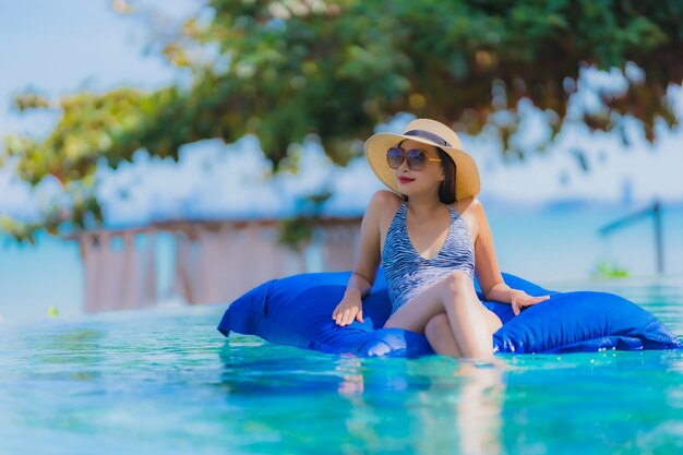 肖像画美しい若いアジア女性の幸せな笑顔は青い空にホテルリゾートニアリー海オーシャンビーチでプールでリラックスします。