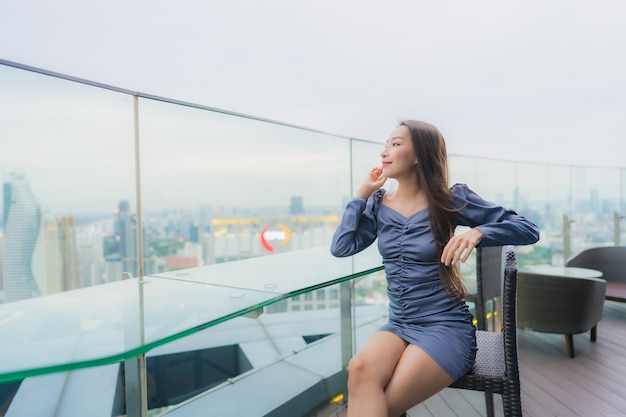 Улыбка красивой молодой азиатской женщины портрета счастливая на ресторане на крыше вокруг вида на город