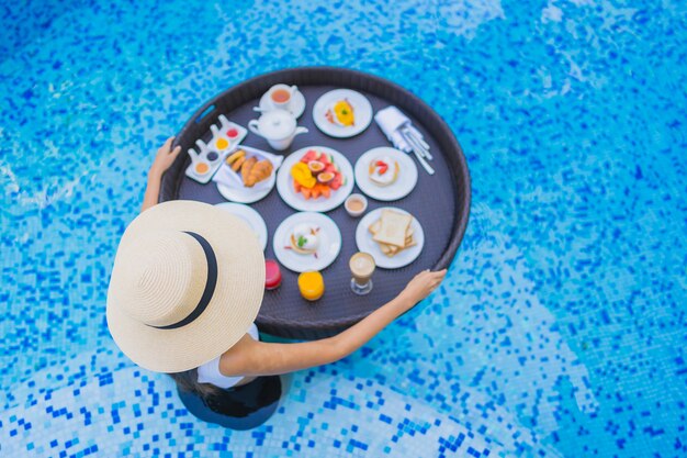 Portrait beautiful young asian woman happy smile with floating breakfast in tray on swimming pool