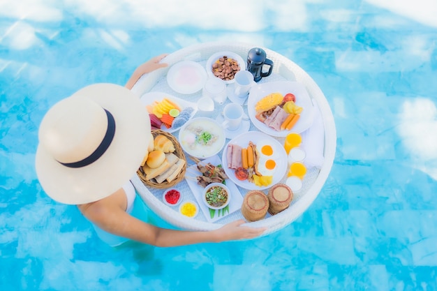 Portrait beautiful young asian woman happy smile with floating breakfast in tray on swimming pool