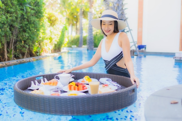 Portrait beautiful young asian woman happy smile with floating breakfast in tray on swimming pool