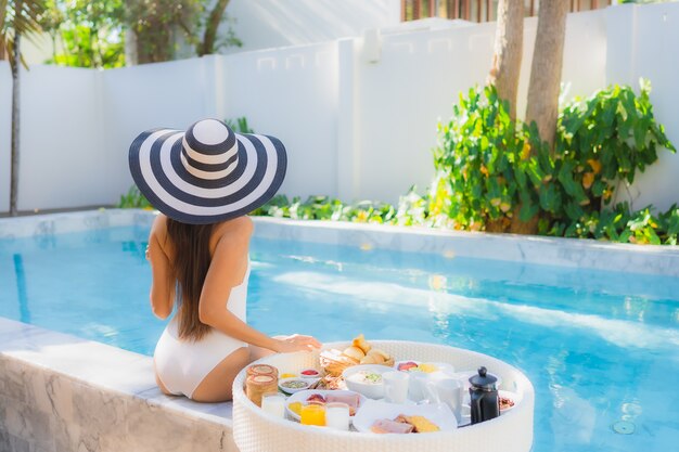 Portrait beautiful young asian woman happy smile with floating breakfast in tray on swimming pool