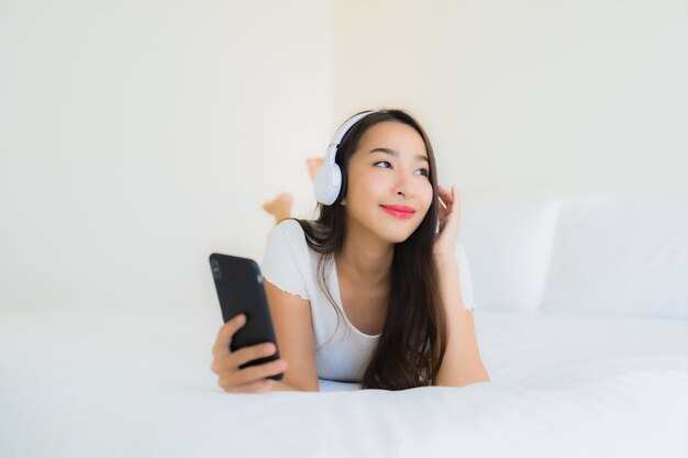 スマート携帯電話とヘッドフォンで音楽を聴くの美しい若いアジア女性の幸せな笑顔の肖像画