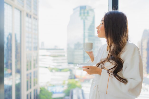 肖像画の美しい若いアジア女性はシティービューのコーヒーカップを保持します。