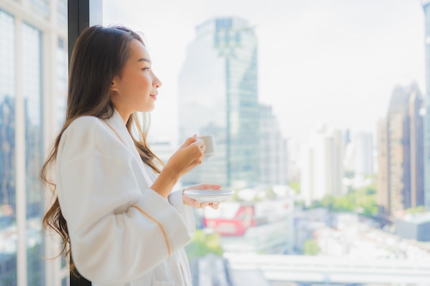 세로 아름 다운 젊은 아시아 여자는 도시 전망 커피 컵을 개최