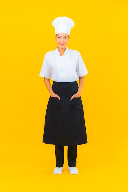 무료 사진 노란색 외진 배경에 모자를 쓴 요리사 또는 요리사 유니폼을 입은 아름다운 젊은 아시아 여성의 초상화