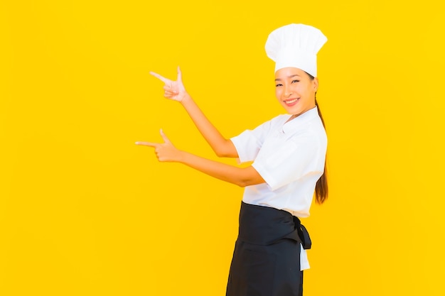 黄色の孤立した背景に帽子とシェフまたは料理の制服を着た美しい若いアジアの女性の肖像画
