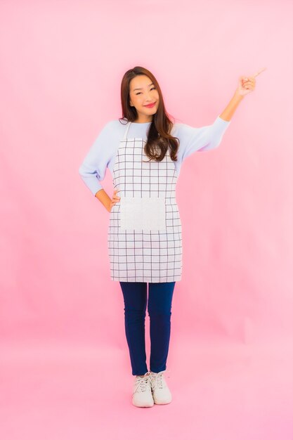 Portrait beautiful young asian woman in kitchen wear with apron on pink isolated wall