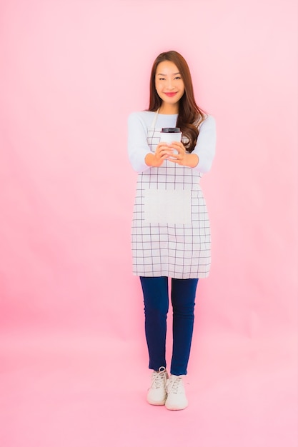 Portrait beautiful young asian woman in kitchen wear with apron on pink isolated wall