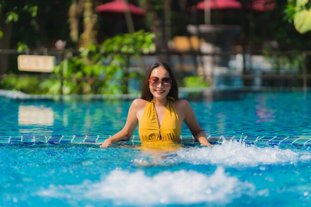 Досуг женщины портрета красивый молодой азиатский ослабляет улыбку и счастливый вокруг бассейна в курорте гостиницы