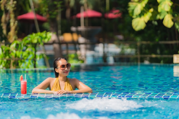 肖像画美しい若いアジア女性レジャーはホテルリゾートのプールの周りのスイカジュースと笑顔をリラックス
