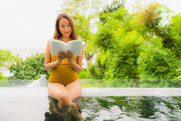 Portrait beautiful young asian woman reading book in swimming pool at hotel and resort