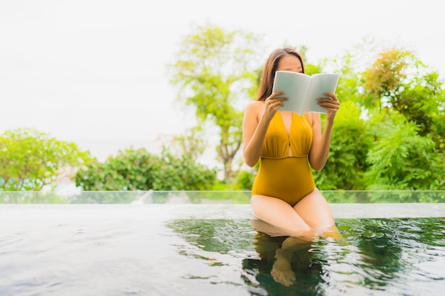 Portrait beautiful young asian woman reading book in swimming pool at hotel and resort