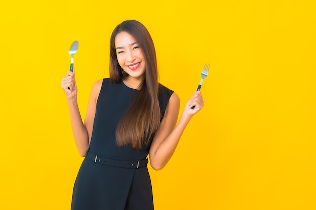 Portrait beautiful young asian woman ready to eat with fork and spoon on yellow background