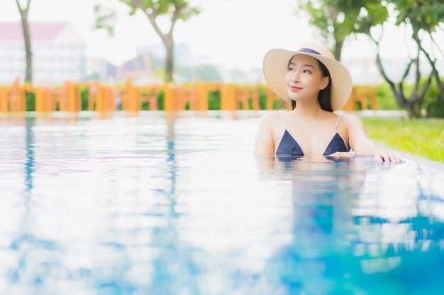 肖像画の美しい若いアジアの女性がリラックスしてレジャー休暇にホテルリゾートの屋外スイミングプールの周りの笑顔を楽しむ