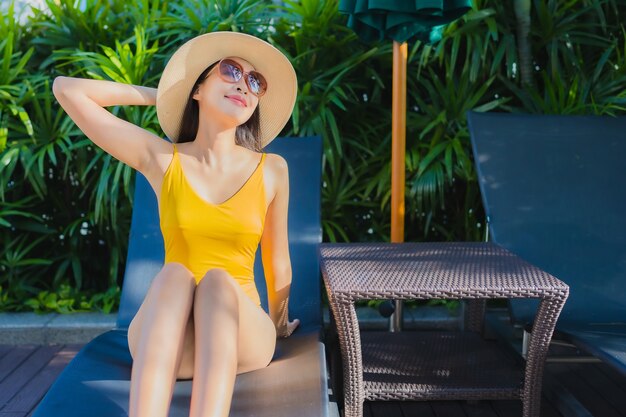 Женщина портрета красивая молодая азиатская ослабляет счастливую улыбку вокруг открытого бассейна в курорте гостиницы на отдыхе