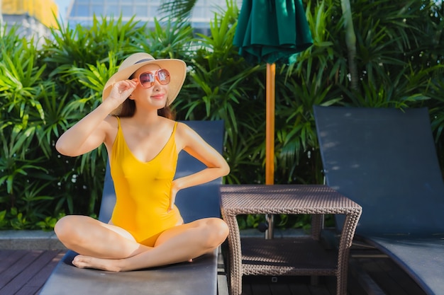 肖像画の美しい若いアジア女性はレジャー休暇のためのホテルリゾートの屋外スイミングプールの周りの幸せな笑顔をリラックスします。