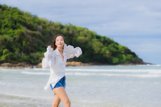 Женщина портрета красивая молодая азиатская ослабляет улыбку вокруг океана моря пляжа в поездке каникул праздника