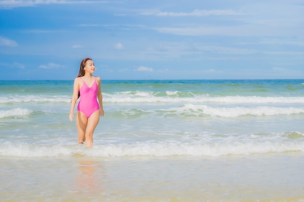 Женщина портрета красивая молодая азиатская ослабляет улыбку вокруг океана моря пляжа в поездке каникул праздника