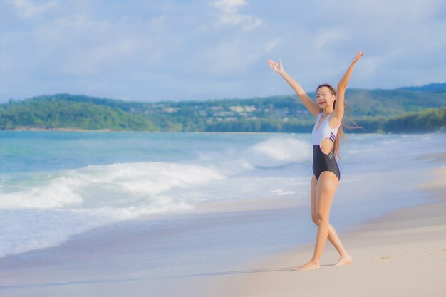 Женщина портрета красивая молодая азиатская ослабляет улыбку вокруг океана моря пляжа в отпуске