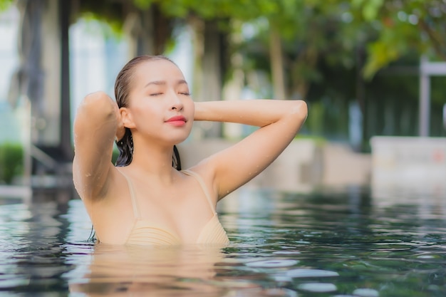 La bella giovane donna asiatica del ritratto si rilassa il sorriso intorno alla piscina all'aperto nella località di soggiorno dell'hotel sul viaggio di vacanza