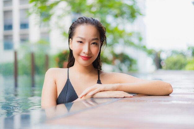 肖像画美しい若いアジアの女性がホテルリゾートの屋外スイミングプールの周りの笑顔をリラックス