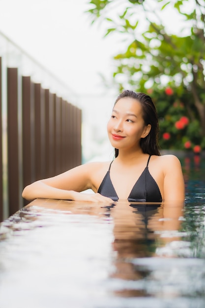 肖像画美しい若いアジアの女性がホテルリゾートの屋外スイミングプールの周りの笑顔をリラックス