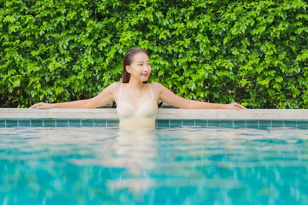 La bella giovane donna asiatica del ritratto si rilassa il sorriso intorno alla piscina all'aperto nella località di soggiorno dell'hotel
