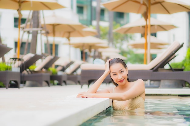 La bella giovane donna asiatica del ritratto si rilassa il sorriso intorno alla piscina all'aperto nella località di soggiorno dell'hotel