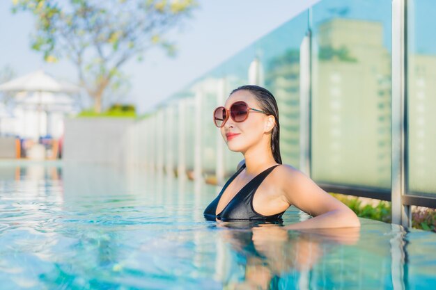 Женщина портрета красивая молодая азиатская ослабляет улыбку вокруг открытого бассейна в курорте гостиницы