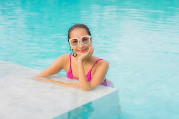 Женщина портрета красивая молодая азиатская ослабляет улыбку вокруг открытого бассейна в курорте гостиницы