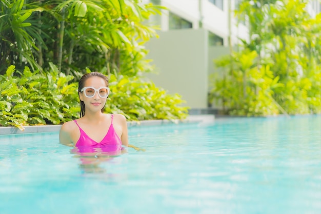 La bella giovane donna asiatica del ritratto si rilassa il sorriso intorno alla piscina all'aperto nella località di soggiorno dell'hotel