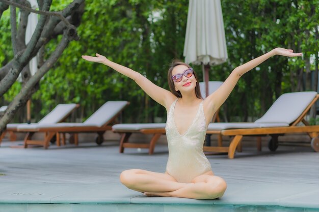 La bella giovane donna asiatica del ritratto si rilassa il sorriso intorno alla piscina all'aperto