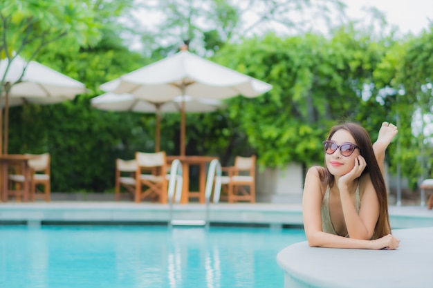 La bella giovane donna asiatica del ritratto si rilassa il sorriso intorno alla piscina all'aperto