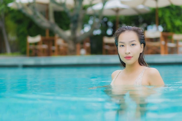 La bella giovane donna asiatica del ritratto si rilassa il sorriso intorno alla piscina all'aperto
