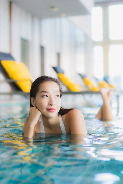 肖像画の美しい若いアジアの女性は、traval休暇でホテルリゾートのスイミングプールの周りの笑顔をリラックスします。
