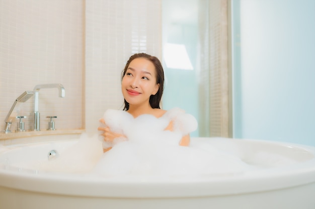 肖像画の美しい若いアジア女性はバスルームのインテリアでバスタブで笑顔をリラックスします。