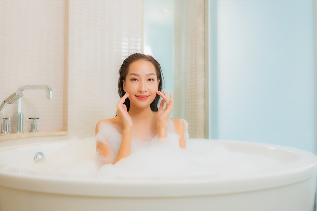 肖像画の美しい若いアジア女性はバスルームのインテリアでバスタブで笑顔をリラックスします。