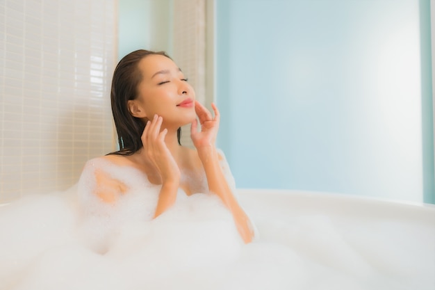 Женщина портрета красивая молодая азиатская ослабляет улыбку в ванне на интерьере ванной комнаты