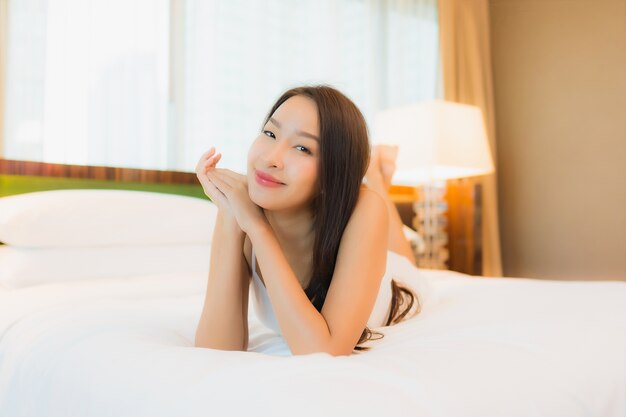 Женщина портрета красивая молодая азиатская ослабляет улыбку на кровати в интерьере спальни