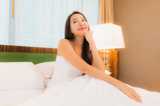 세로 아름 다운 젊은 아시아 여자 침실 인테리어에 침대에 미소를 긴장