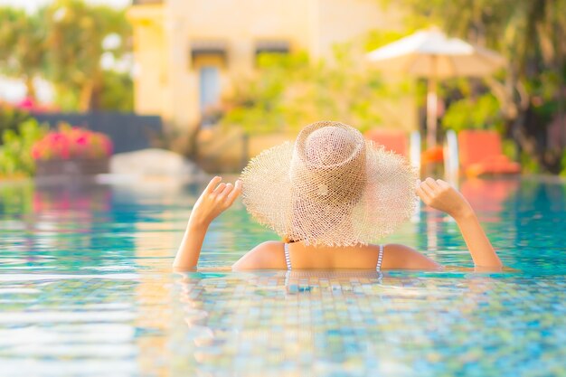 Женщина портрета красивая молодая азиатская ослабляет улыбку наслаждается отдыхом вокруг бассейна в курортном отеле на каникулах