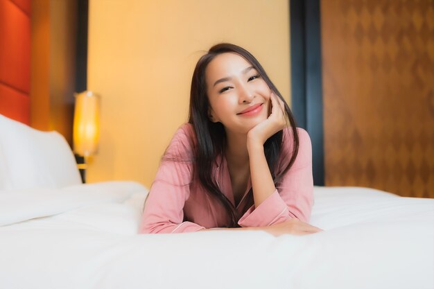 肖像画の美しい若いアジア女性は寝室のインテリアのベッドで幸せな笑顔をリラックス