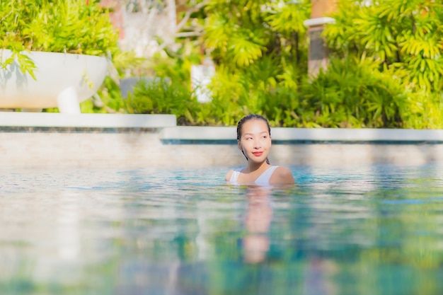 肖像画美しい若いアジアの女性は休暇旅行でホテルリゾートの屋外スイミングプールの周りの笑顔のレジャーをリラックス