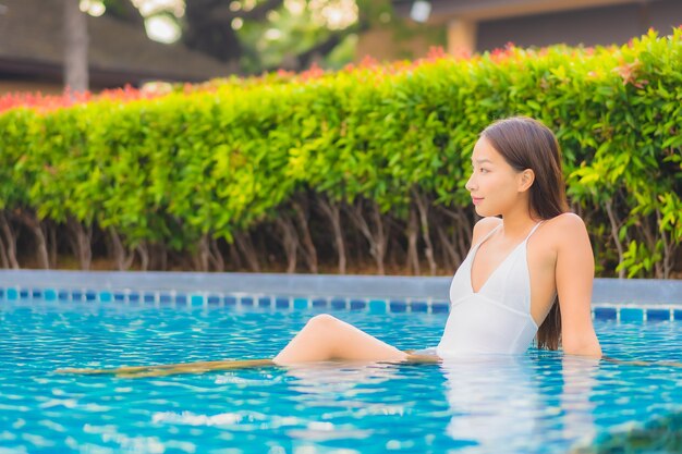 La bella giovane donna asiatica del ritratto si rilassa il tempo libero di sorriso intorno alla piscina all'aperto quasi il mare