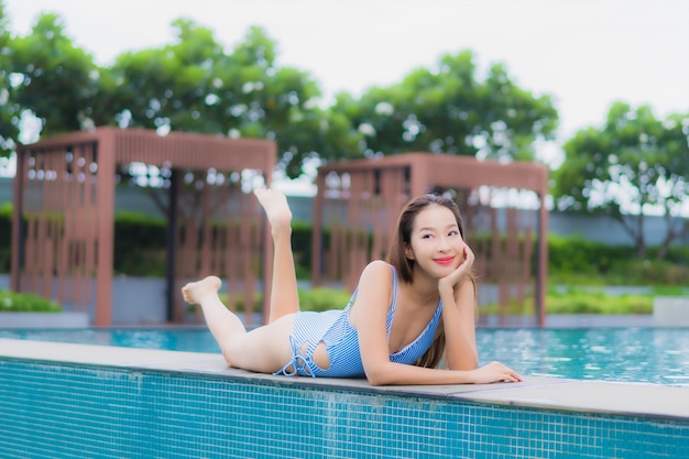 美しい若いアジアの女性の肖像画は屋外スイミングプールの周り笑顔レジャーをリラックスします。