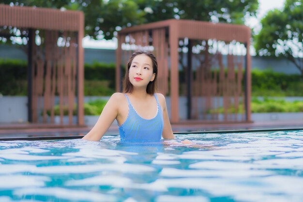 美しい若いアジアの女性の肖像画は屋外スイミングプールの周り笑顔レジャーをリラックスします。